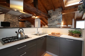 Una cucina moderna con parete in pietra, travi in legno, piano cottura a gas e televisore a schermo piatto.