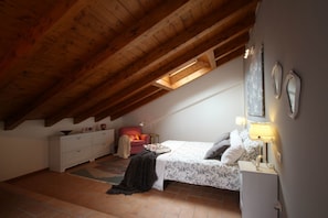 Una camera da letto con soffitto spiovente, un letto, un comodino, una cassettiera, una sedia e una finestra.