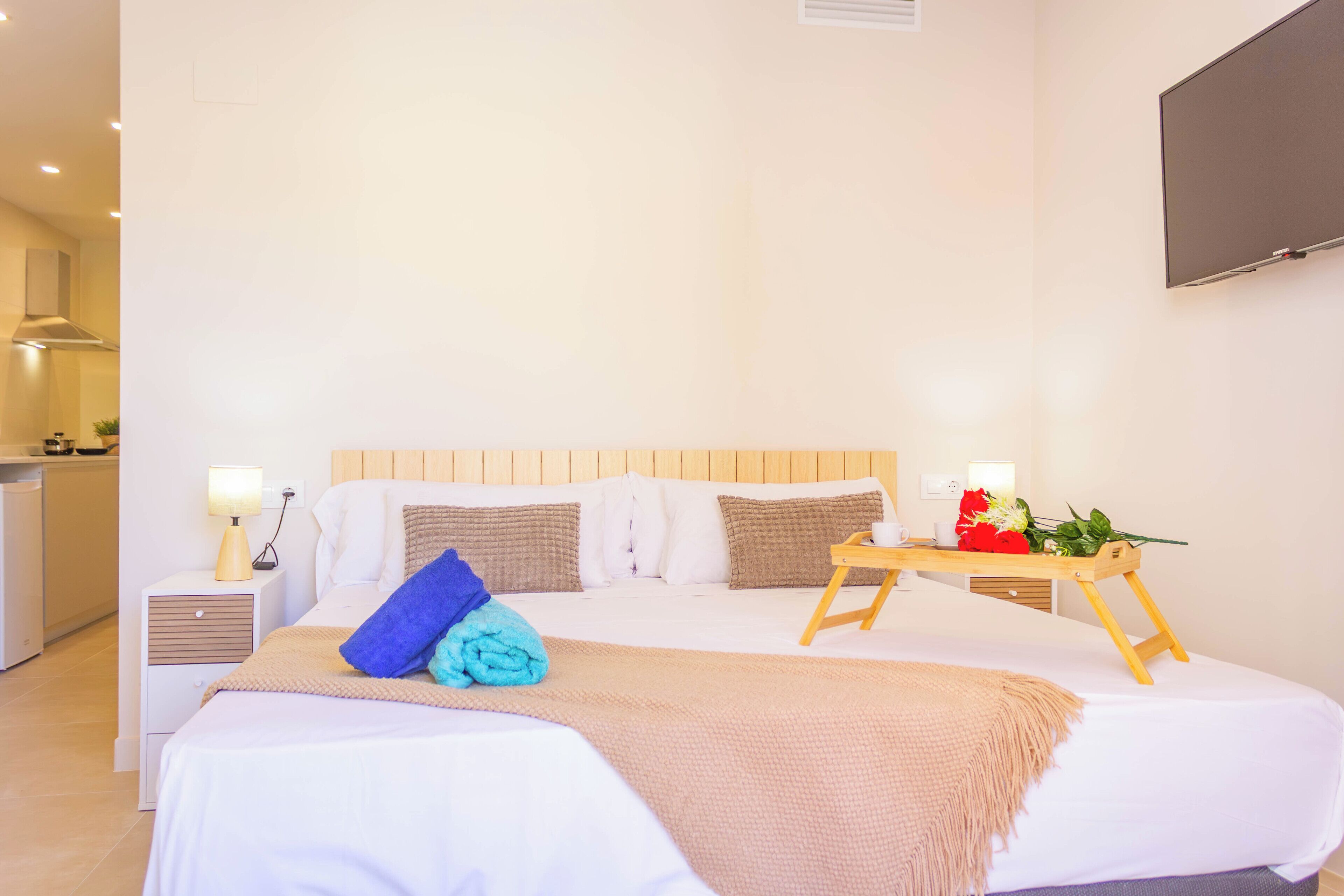 A neatly arranged hotel room with a bed, bedside tables, a TV, and a small table with a flower arrangement.