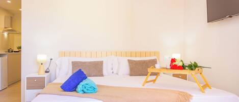 A neatly arranged hotel room with a bed, bedside tables, a TV, and a small table with a flower arrangement.