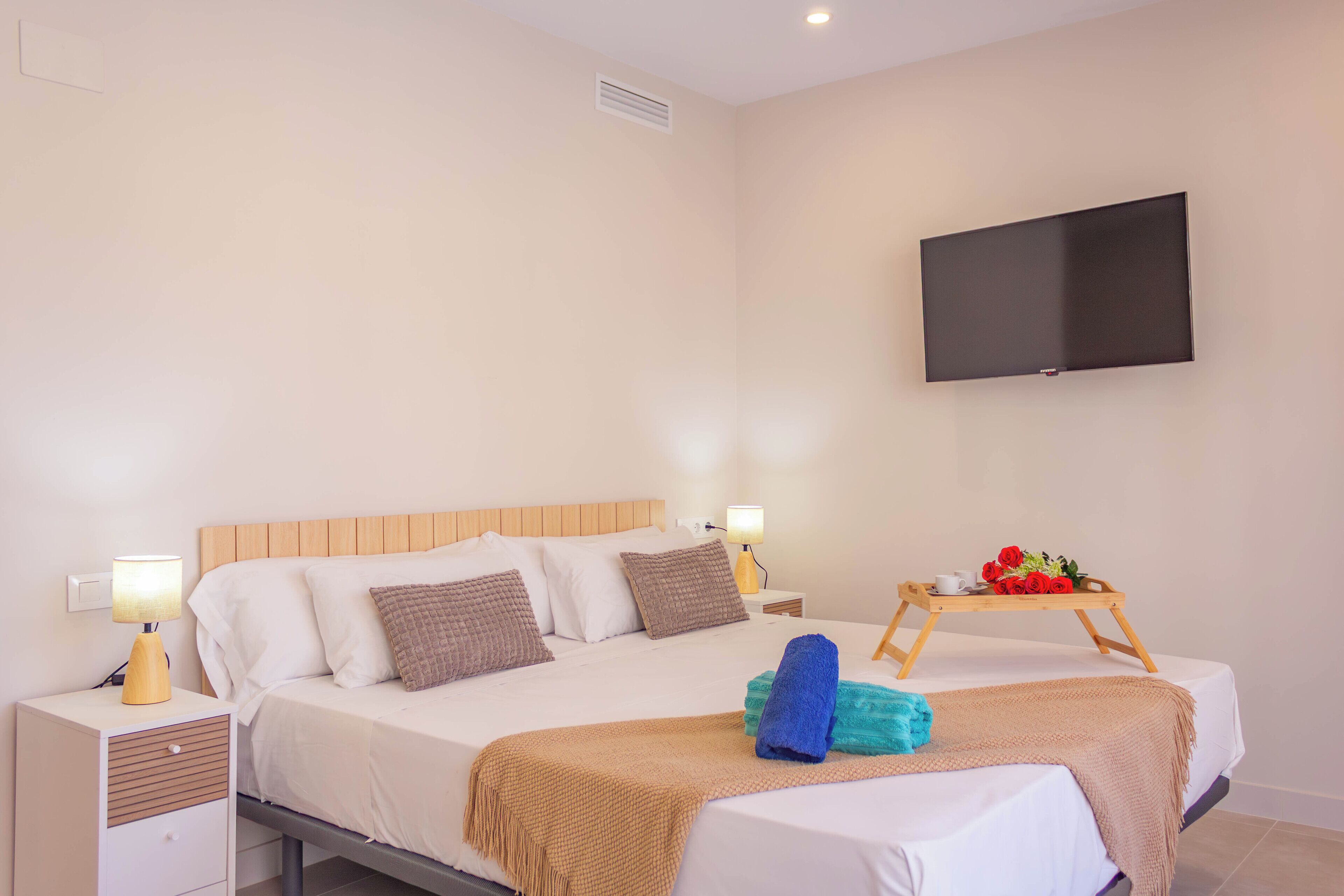A hotel room with a bed, bedside tables, a TV, and a tray with flowers.