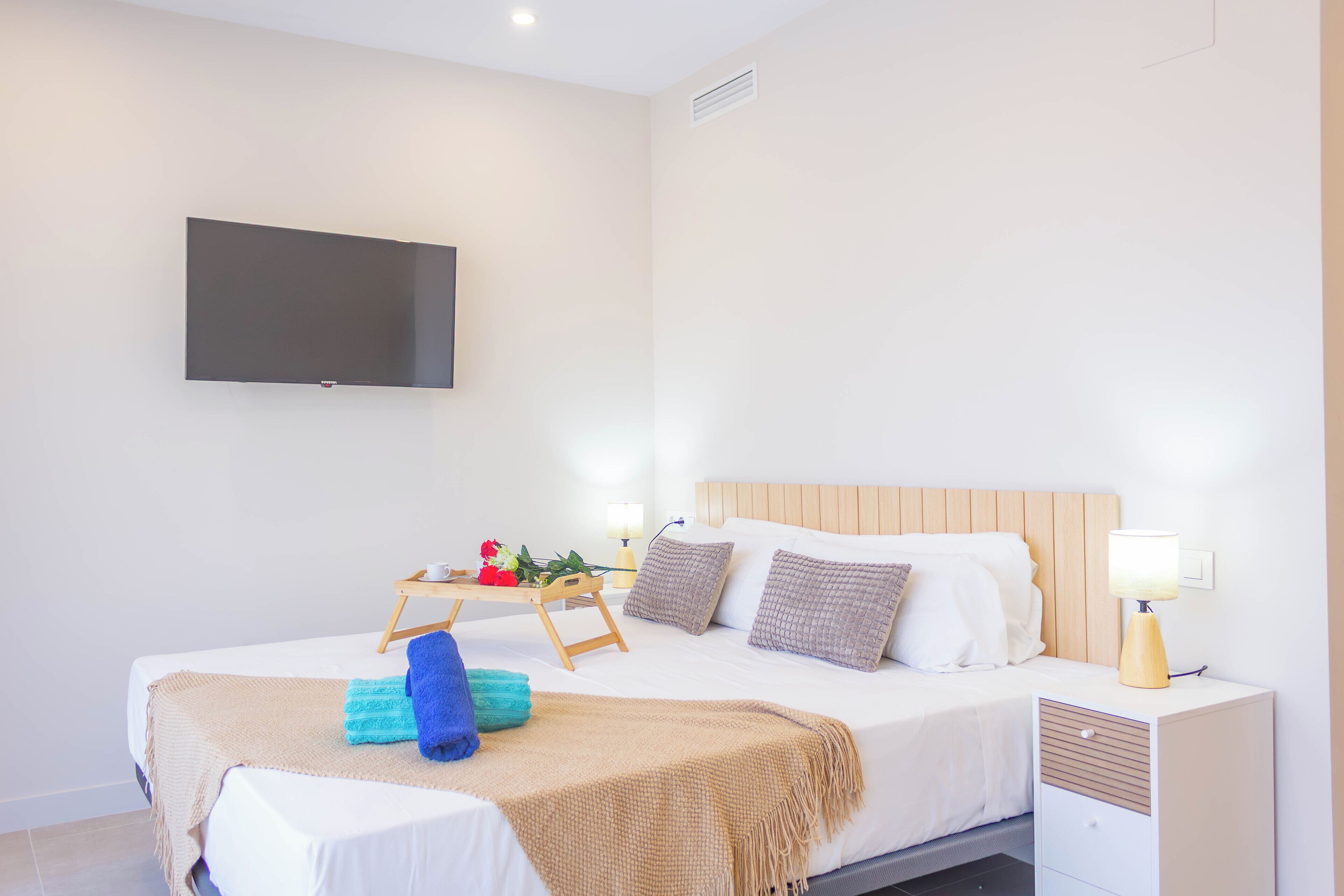 Una habitación de hotel moderna con cama, mesita de noche, lámpara y televisión montada en la pared.