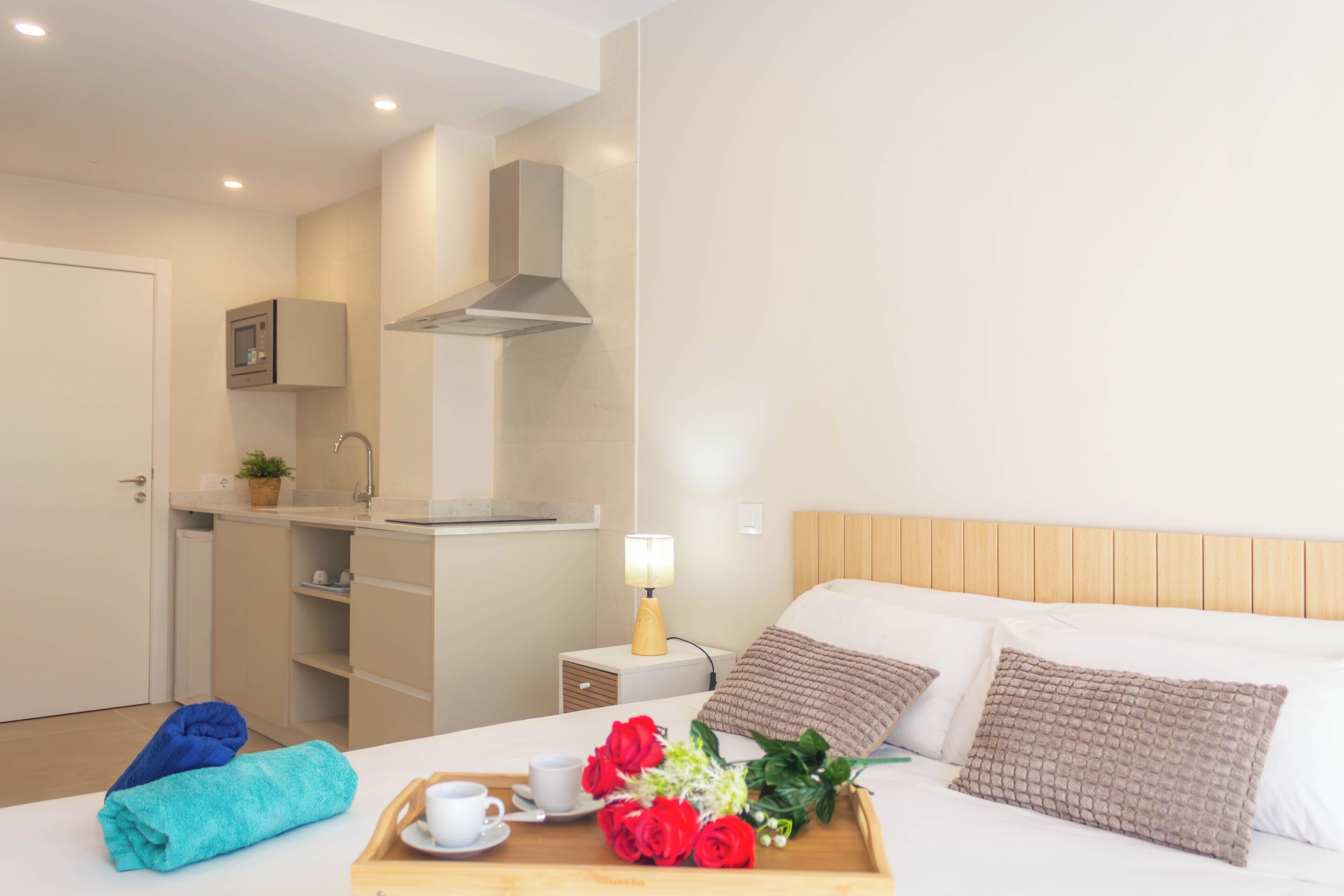 Une chambre d’hôtel avec un lit, une table de chevet, une lampe et un plateau contenant une tasse, des serviettes et des fleurs.