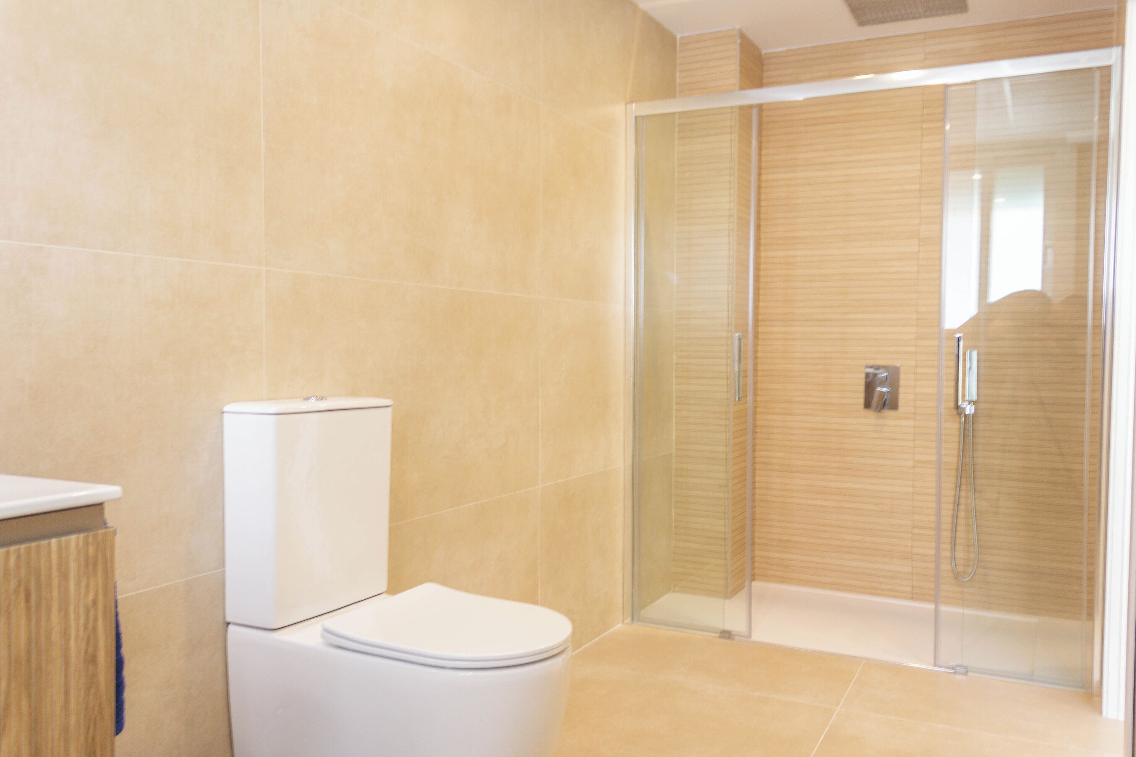 A modern bathroom with a toilet, a glass shower enclosure, and beige tiled walls.