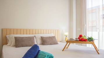 A neatly made bed with two pillows, a folded towel, and a tray table with a cup, a saucer, and a bouquet of red roses.