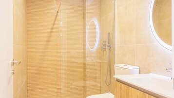 Un baño moderno con ducha envuelta en vidrio, inodoro y lavamanos con espejo.