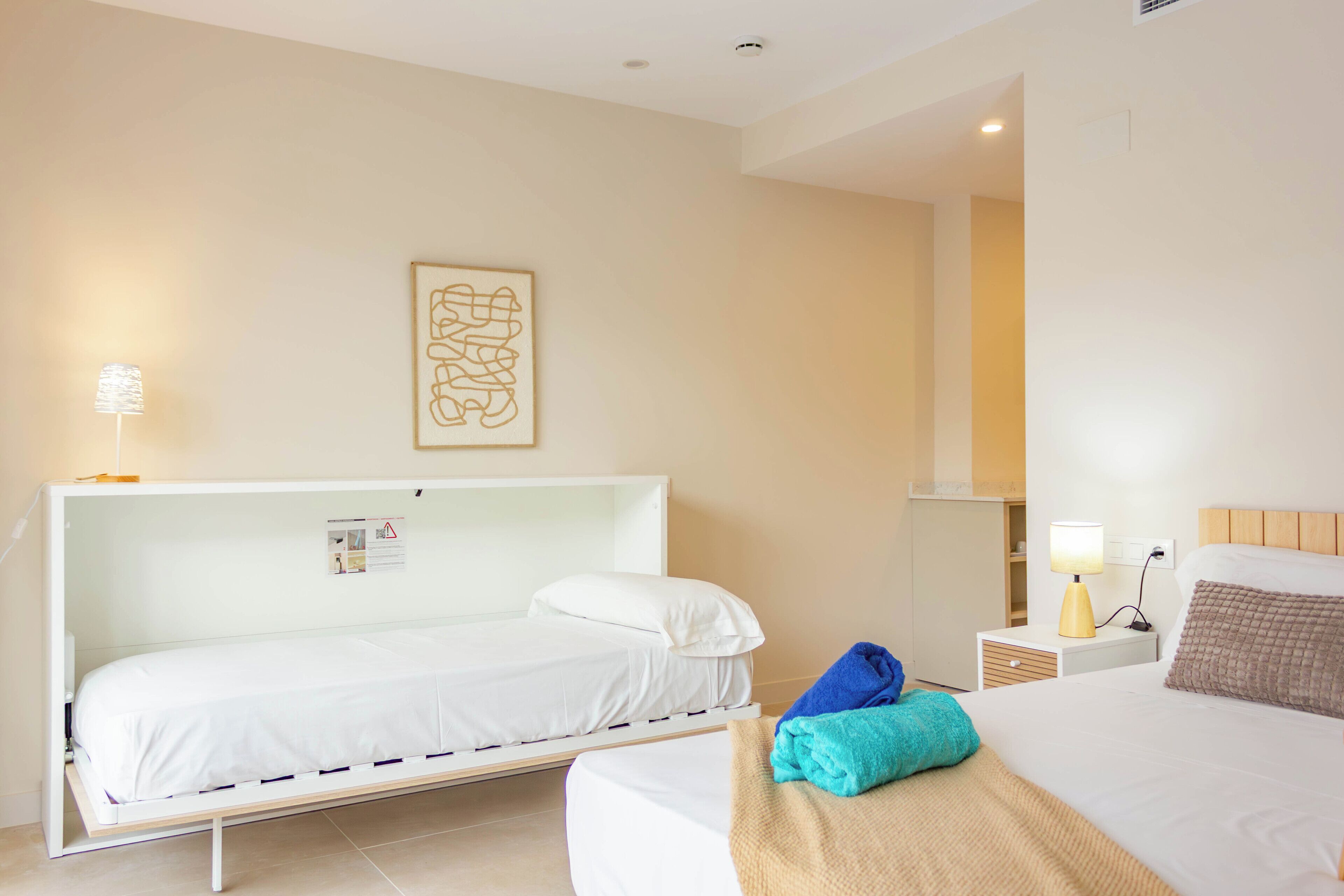 Habitación de hotel con dos camas, una mesita de noche con lámpara, una obra de arte en la pared y un mueble pequeño.