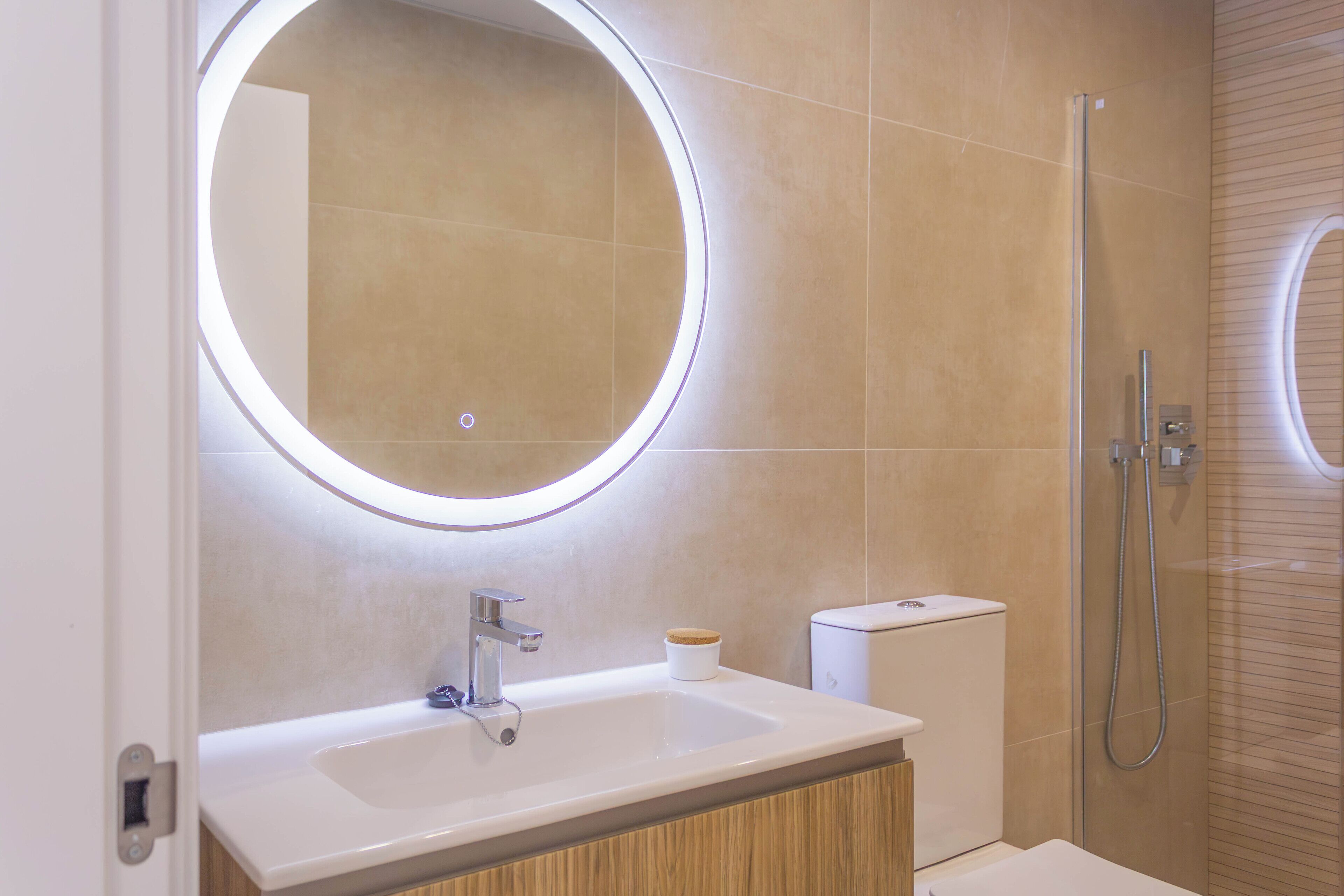 Un bany modern amb un mirall rodó, un lavabo i una dutxa.