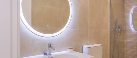 Un bany modern amb un mirall rodó, un lavabo i una dutxa.