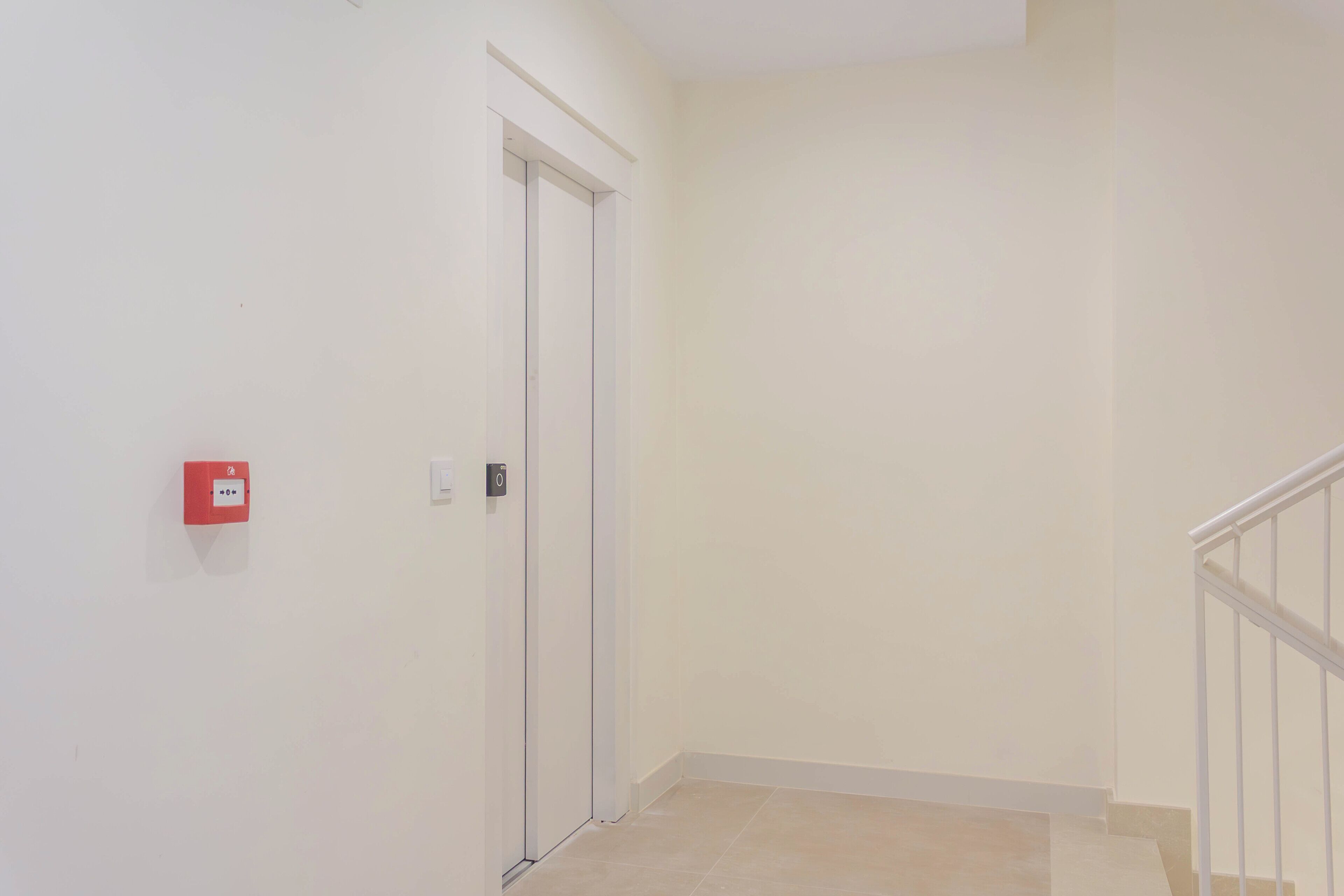 Un pasillo con una puerta cerrada, un extintor rojo y una barandilla blanca.