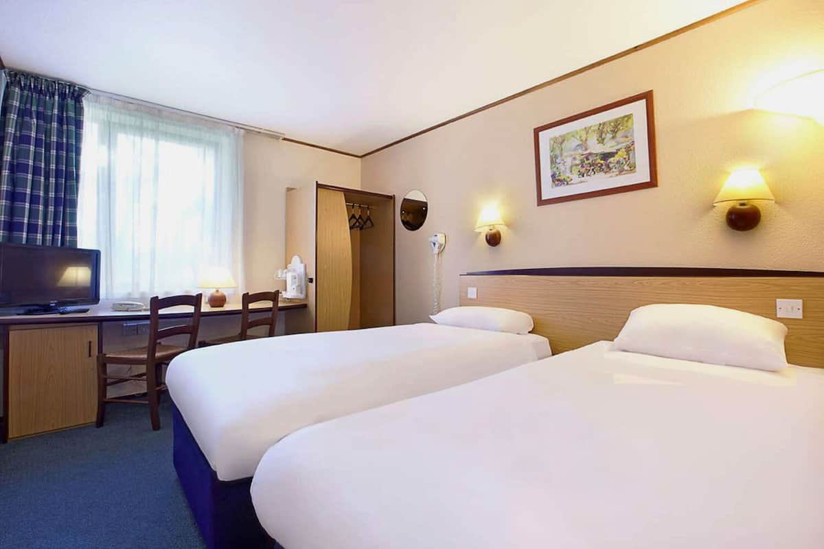 A hotel room with two beds, a desk with a chair, a television, and a painting on the wall.