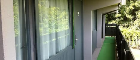A corridor with a green carpet, a window with a curtain, and a door with a green handle.