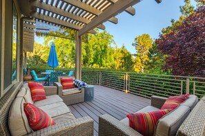 An outdoor deck with wicker furniture, a blue umbrella, and a view of trees.