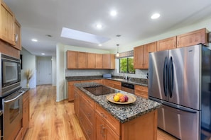 A modern kitchen with wooden cabinets, granite countertops, a stainless steel refrigerator, and a built-in oven.