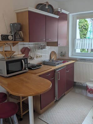 Une cuisine de taille réduite, équipée d’un four à micro-ondes, d’un comptoir en bois et de placards rouges.