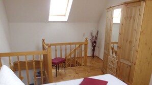 A bedroom with a wooden bed, a red pillow, a wooden chair, a wooden wardrobe, and a skylight.