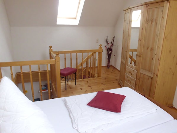 A bedroom with a wooden bed, a red pillow, a wooden chair, a wooden wardrobe, and a skylight.