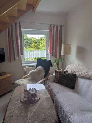Une chambre à coucher avec un lit, une chaise, une table, une lampe et une fenêtre avec des rideaux.
