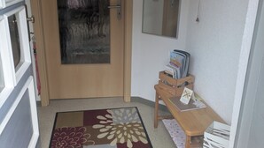 A hallway with a wooden door, a small table with books, a mirror, and a patterned rug.