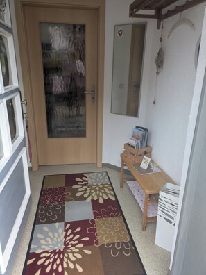 A hallway with a wooden door, a small table with books, a mirror, and a patterned rug.