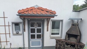 A patio with a brick floor, a stone barbecue grill, a table with chairs, and a door with a window.