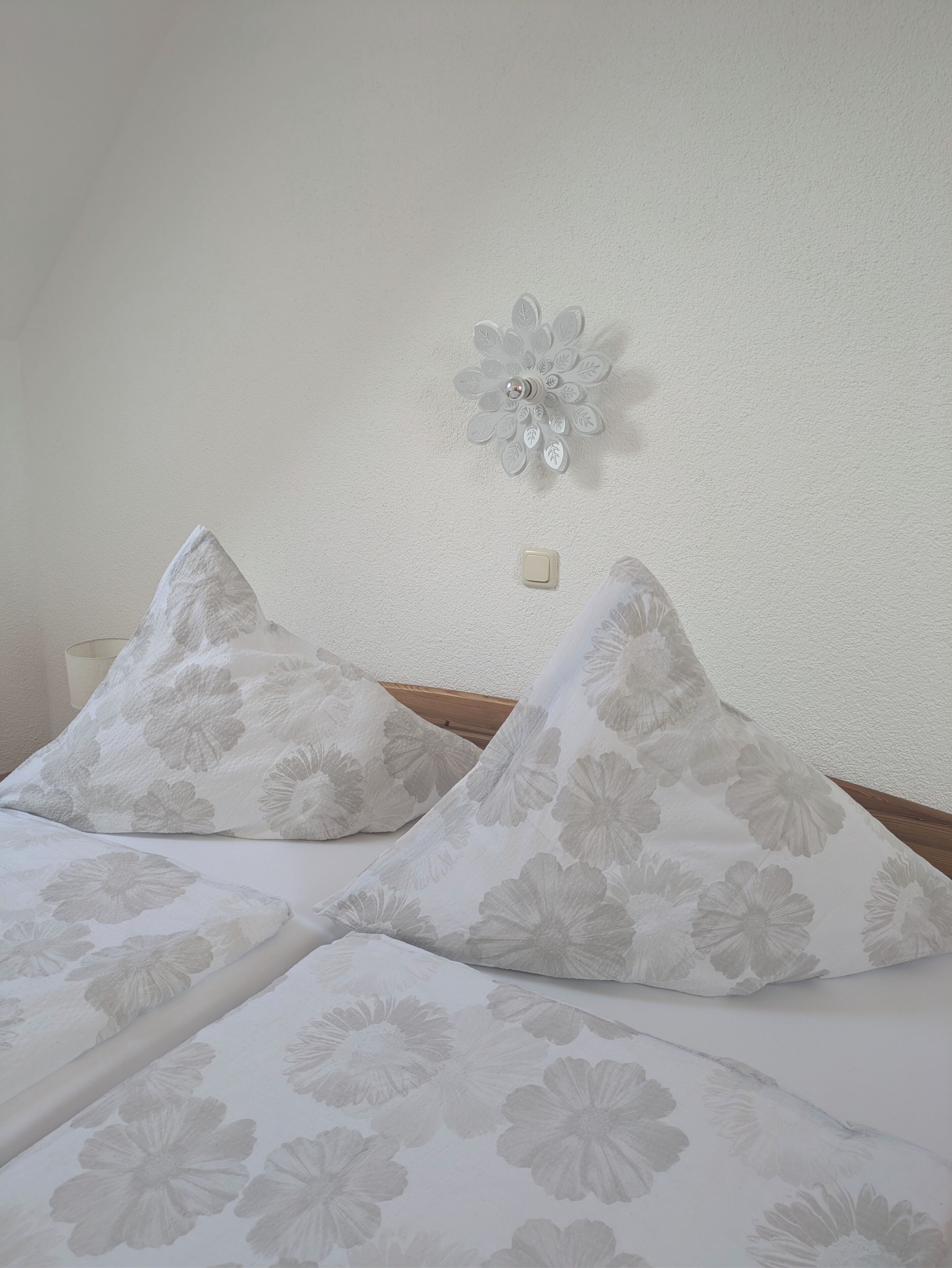 A bed with floral-patterned bedding, a wall-mounted light fixture, and a power outlet.