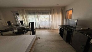 A compact hotel room with a bed, a small table, a TV, and a kitchenette.