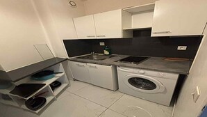 A compact kitchen with white cabinets, a built-in washing machine, and a sink.