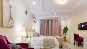 A modern hotel room with a bed, a desk, a chair, a TV, and a large window with curtains.