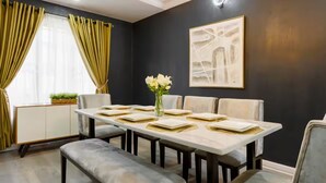 A dining area with a long table set for six, a bench, and a vase with flowers.