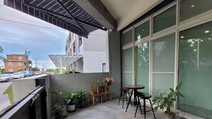 A balcony with potted plants, a wooden table, and two black stools.