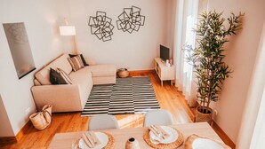 A modern living room with a sofa, dining table set for four, a TV, and a large plant. - Chic & Classy Lisboa by GT House (Lisbon)