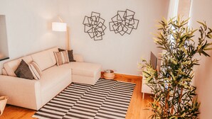 A living room with a beige sofa, a black and white striped rug, a wooden floor, and a large plant. - Chic & Classy Lisboa by GT House (Lisbon)