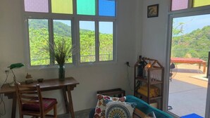 A room with a wooden desk, a chair, a sofa with patterned cushions, and a large window with multiple panes. - Boho-Luxe Pool Villa with Simply Amazing Views by Setting Sun Boutique Homes (ตำบล เกาะลันตาใหญ่)