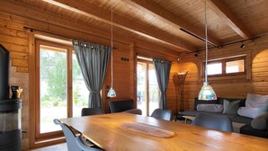 Een houten blokhut van binnen met een eettafel, stoelen, een bank en een open haard.