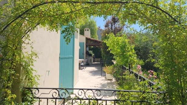 A pathway leading to a building with a blue door, surrounded by greenery and a metal fence. - Peace of mind (Saint-Cézaire-sur-Siagne)