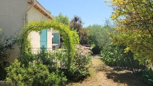 A narrow pathway flanked by lush greenery and a building with a tiled roof and blue shutters. - Peace of mind (Saint-Cézaire-sur-Siagne)