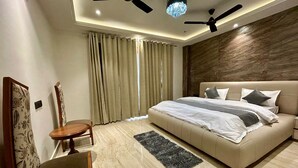 A modern bedroom with a large bed, two ceiling fans, a chandelier, and a view of the outdoors through curtains. - Ganga Euphoria Villa (Rishikesh)