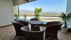 A balcony with wicker furniture and potted plants, overlooking a scenic landscape. - Ganga Euphoria Villa (Rishikesh)