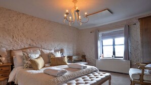 Une chambre à coucher avec un grand lit, un banc, une table de chevet, une commode et une fenêtre avec des rideaux.