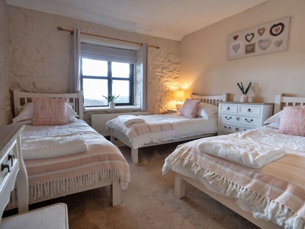 A cozy bedroom with three beds, a stone wall, a window, and a wall-mounted heart decoration.