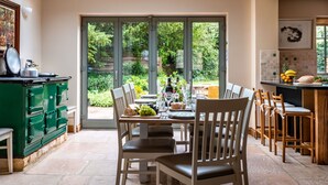 Ein Essbereich mit Tisch für vier Personen, einem grünen Herd und Blick auf den Garten durch große Glastüren.