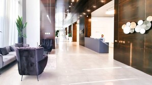 A modern lobby with a sofa, a dark armchair, and potted plants. - Hayarkon Royal in Tel Aviv-yafo (Tel Aviv)