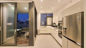 A modern kitchen with a stainless steel refrigerator, a window with blinds, and a dining area with a table and chairs. - Hayarkon Bronze in Tel Aviv-yafo (Tel Aviv)