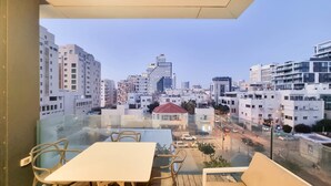 A balcony with a table and chairs, overlooking a cityscape with various buildings and a clear sky. - Hayarkon Bronze in Tel Aviv-yafo (Tel Aviv)