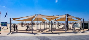 Un espacio de acondicionamiento físico en la playa, con equipamiento deportivo y estructuras con sombra.