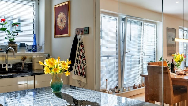 Et moderne køkken med en marmor bordplade, en vase med gule blomster og et spiseområde med et træbord og stole.