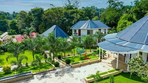 Un resort con varias edificaciones, incluyendo una casa grande de techo azul y una construcción más pequeña con techo rojo. La propiedad cuenta con un césped cuidado, varios árboles y un camino pavimentado.