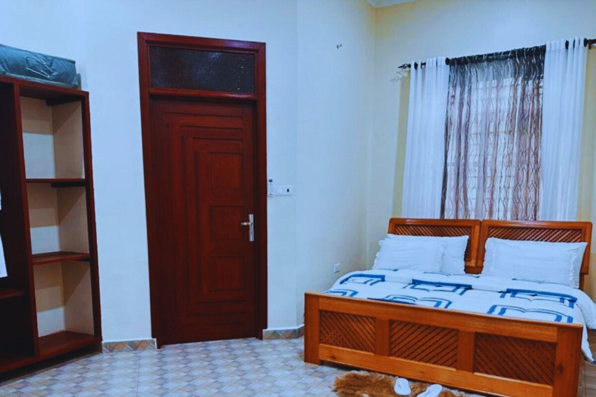 A bedroom with a wooden bed, a wardrobe, and a tiled floor.