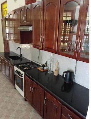 A kitchen with wooden cabinets, a black countertop, a stove, and a sink.